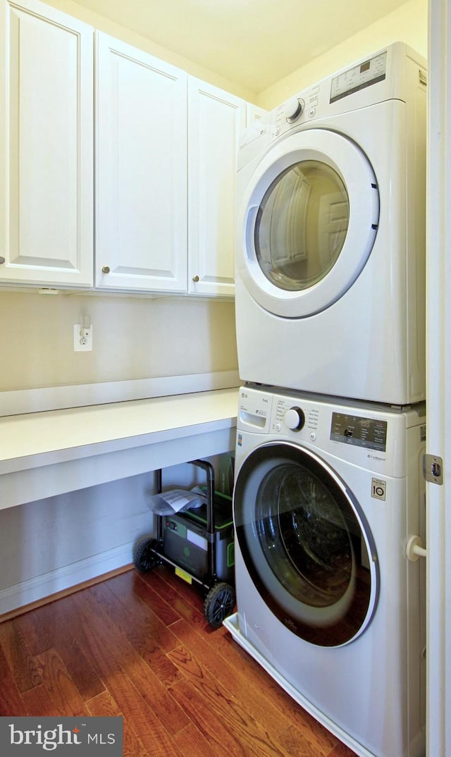 laundry room featuring cabinet space, stacked washer and clothes dryer, and wood finished floors