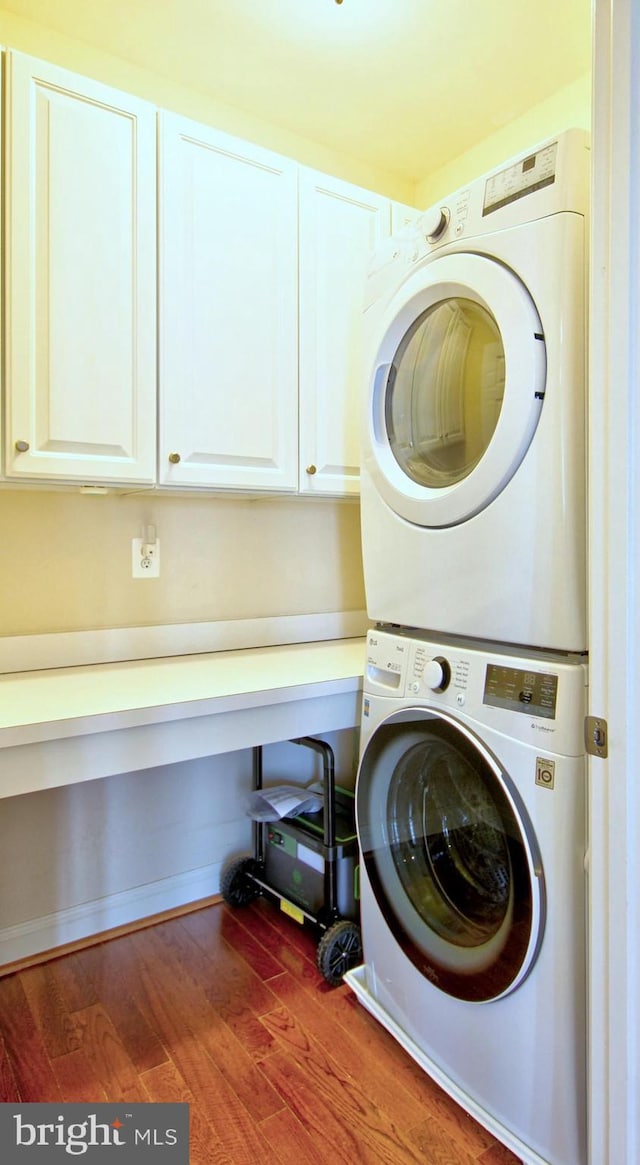 laundry area featuring cabinet space, stacked washing maching and dryer, and wood finished floors