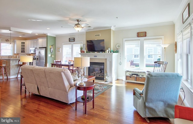 living area with hardwood / wood-style floors, crown molding, plenty of natural light, and a glass covered fireplace