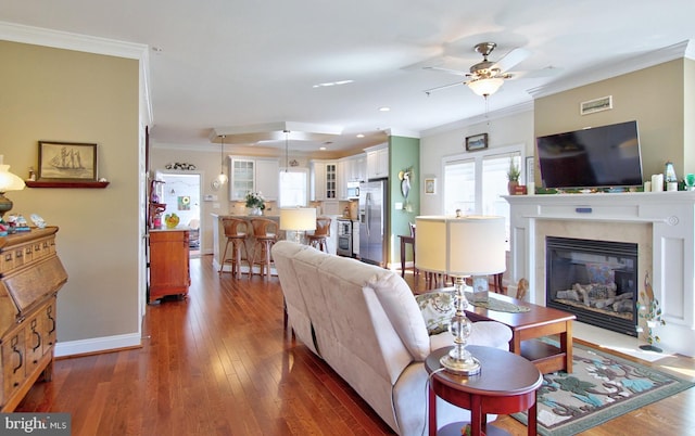 living room with baseboards, ornamental molding, a glass covered fireplace, a ceiling fan, and wood-type flooring