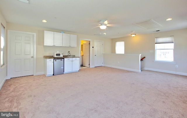 kitchen featuring white microwave, white cabinetry, light carpet, and a sink