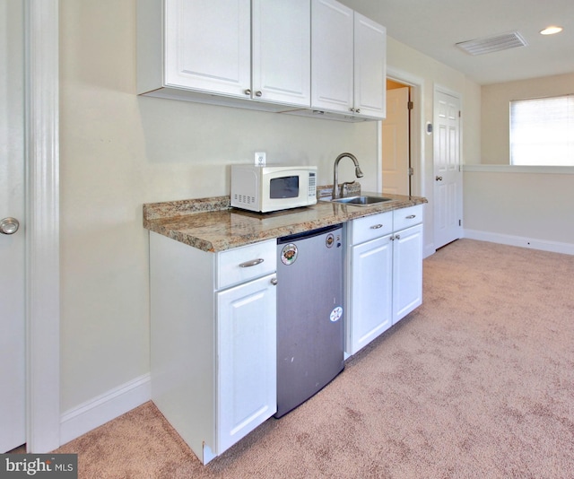 kitchen featuring light carpet, a sink, refrigerator, white cabinets, and white microwave