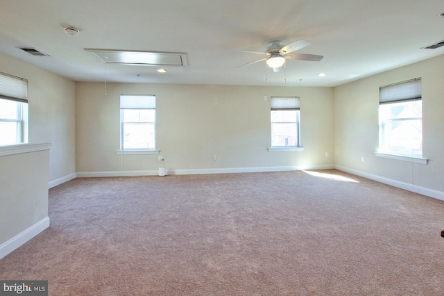 carpeted spare room with visible vents, ceiling fan, attic access, and baseboards