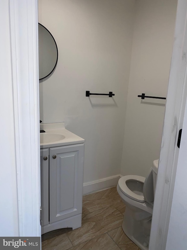 half bath featuring toilet, vanity, and baseboards