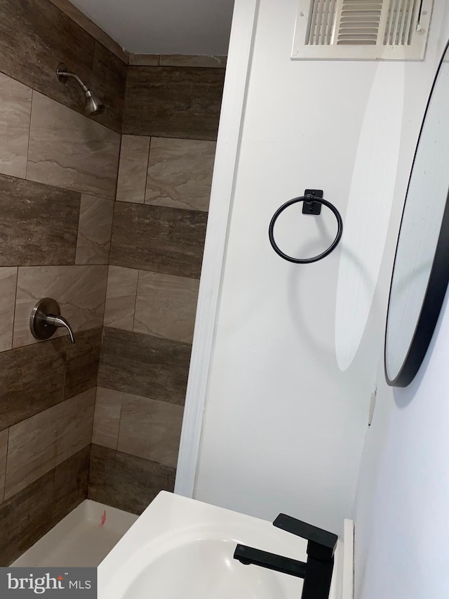 full bathroom with visible vents, a tile shower, and a sink