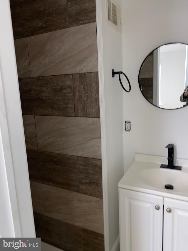 bathroom featuring visible vents, a tile shower, and vanity