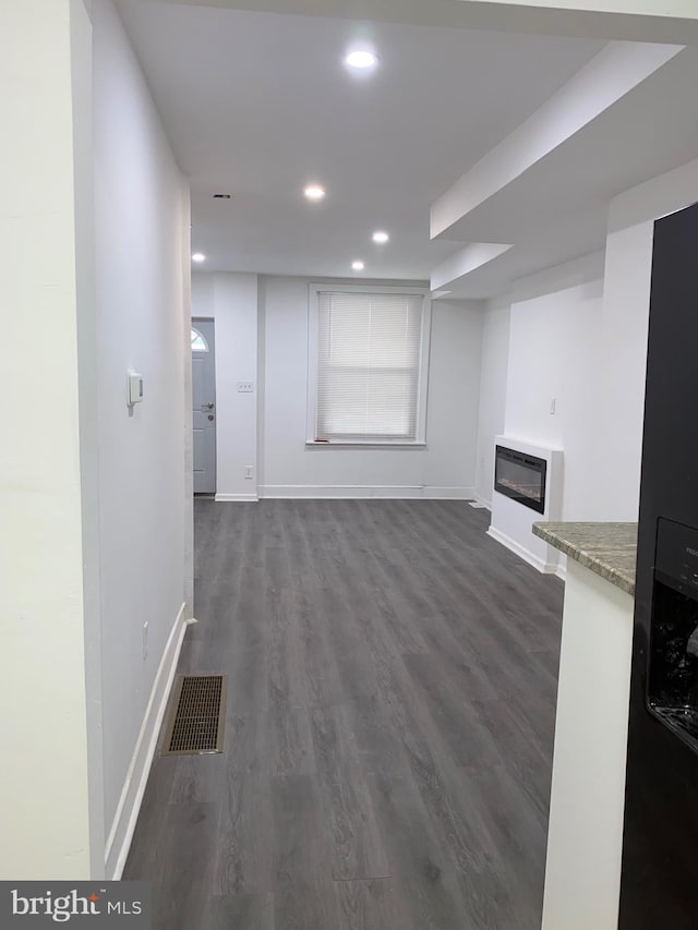 unfurnished living room featuring visible vents, dark wood finished floors, baseboards, a glass covered fireplace, and recessed lighting