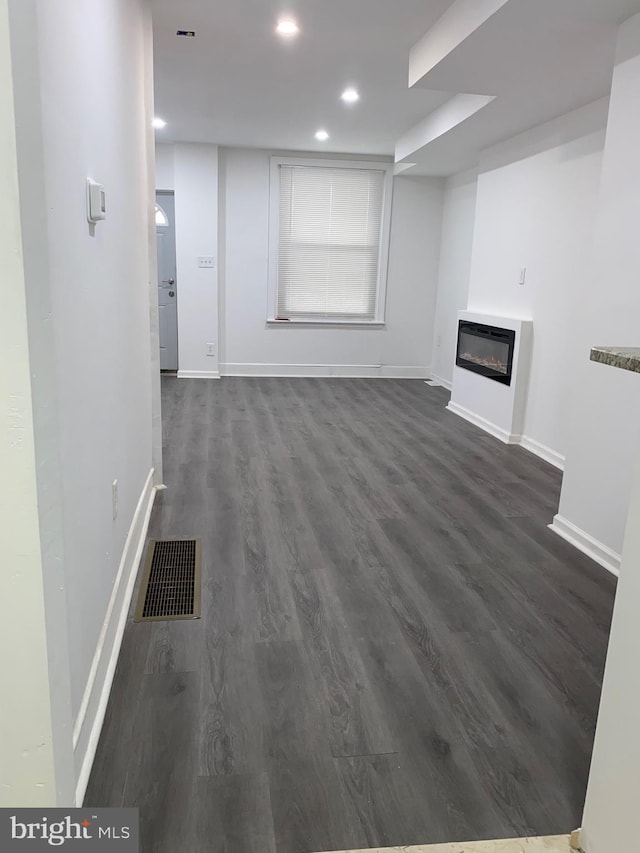 unfurnished living room with baseboards, visible vents, dark wood-type flooring, and a glass covered fireplace