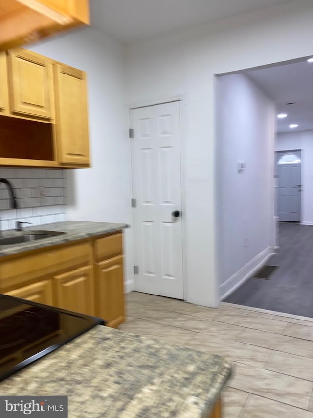 kitchen featuring baseboards, decorative backsplash, stove, light brown cabinets, and a sink