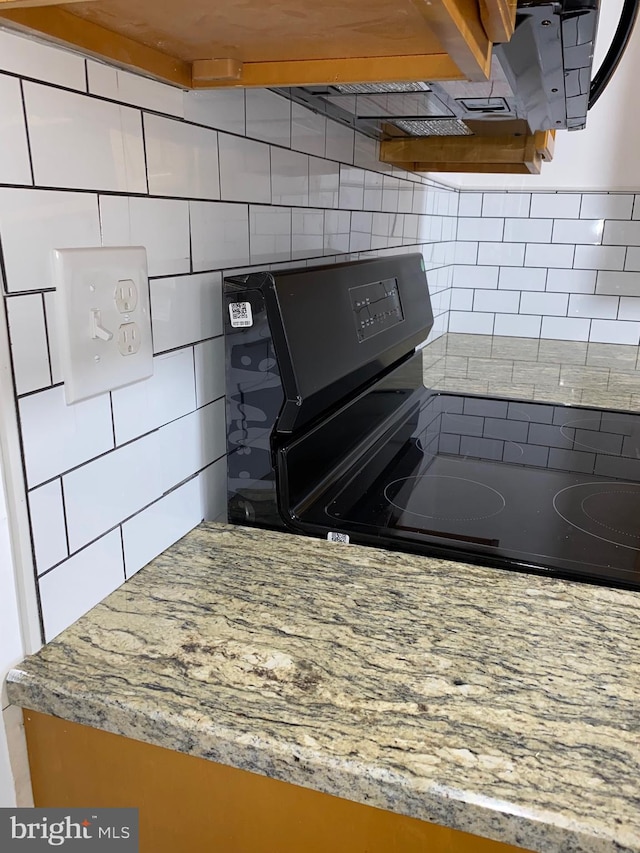 kitchen with black / electric stove, light stone countertops, and decorative backsplash