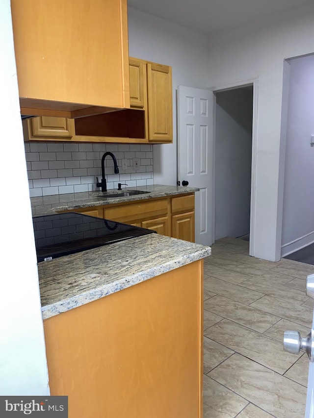 kitchen featuring light brown cabinetry, tasteful backsplash, a sink, and light stone counters