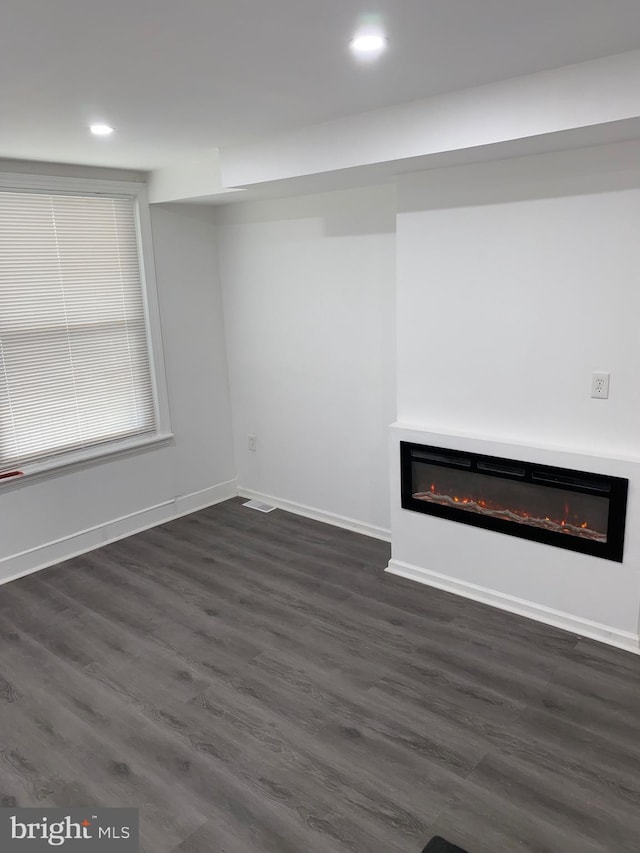 unfurnished living room with baseboards, dark wood-style flooring, a glass covered fireplace, and recessed lighting