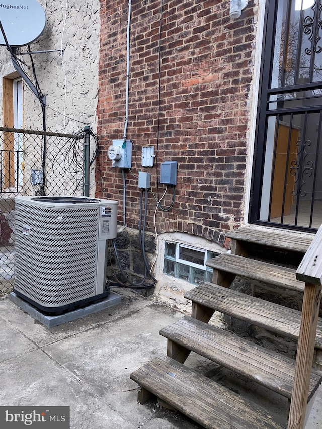 details featuring brick siding, entry steps, central AC, fence, and electric meter