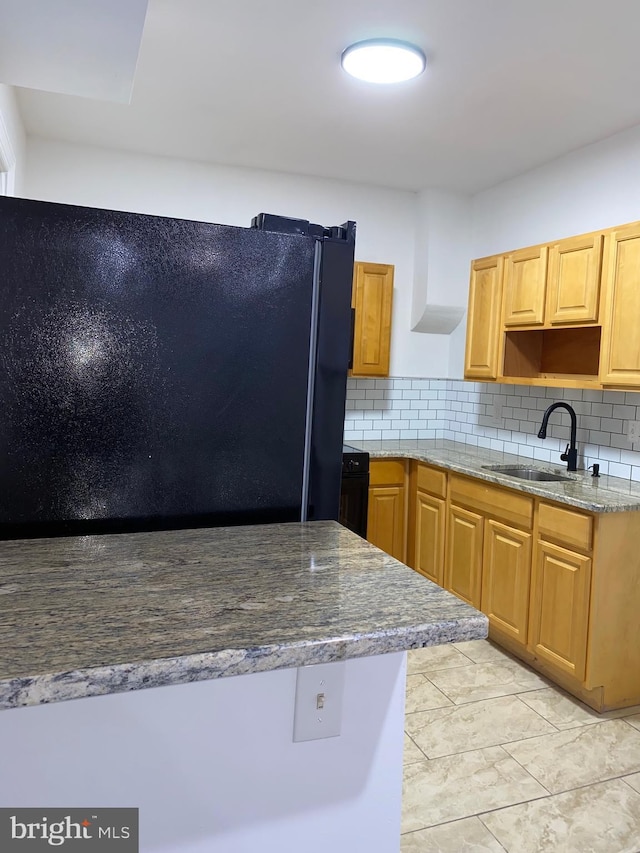 kitchen featuring tasteful backsplash, freestanding refrigerator, stone countertops, and a sink