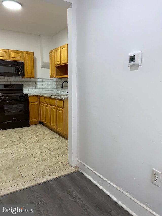 kitchen featuring light wood finished floors, decorative backsplash, a sink, black appliances, and baseboards