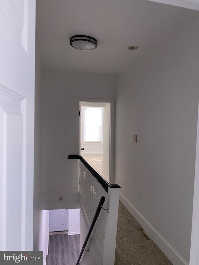 hallway featuring visible vents, baseboards, and an upstairs landing