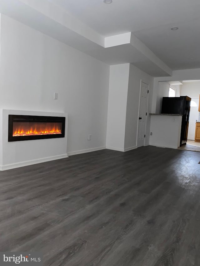 unfurnished living room with a glass covered fireplace, dark wood finished floors, and baseboards