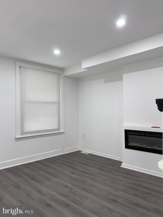 finished basement with a glass covered fireplace, dark wood-style flooring, baseboards, and recessed lighting