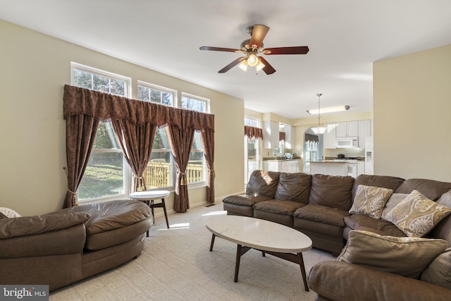 living area featuring a ceiling fan, baseboards, and light carpet