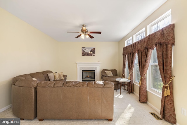 living area with visible vents, baseboards, a premium fireplace, and a ceiling fan