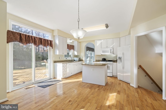 kitchen with white appliances, a kitchen island, white cabinets, and light wood finished floors