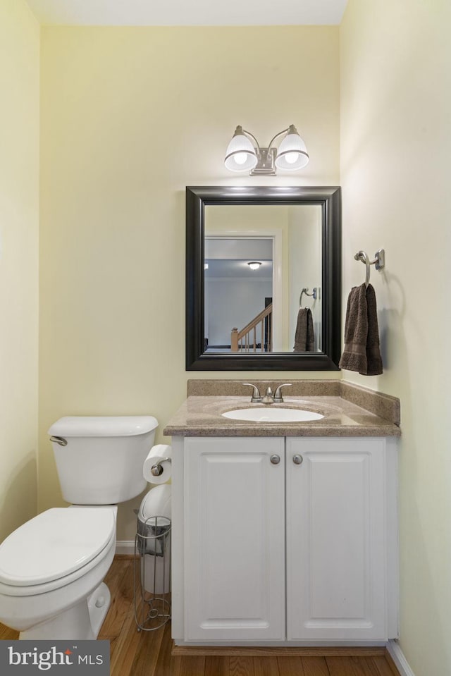 half bath featuring baseboards, toilet, wood finished floors, and vanity