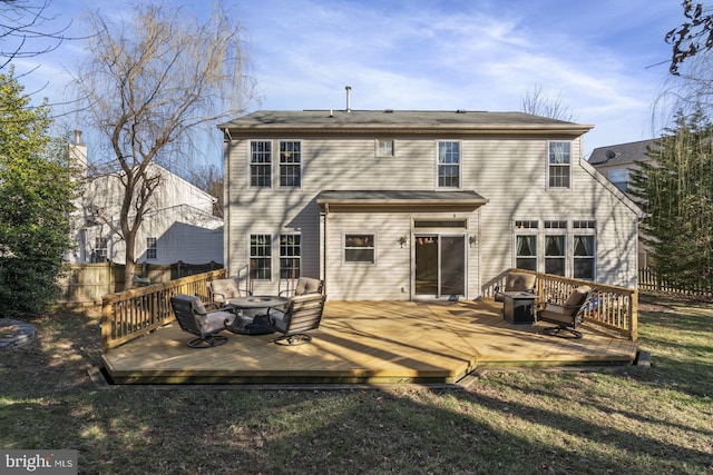 rear view of property featuring a fire pit, a wooden deck, a yard, and fence