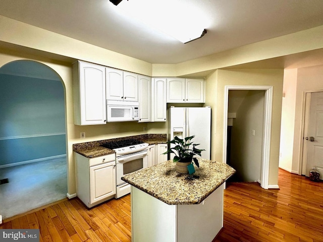 kitchen with white appliances, dark stone countertops, arched walkways, white cabinets, and wood-type flooring