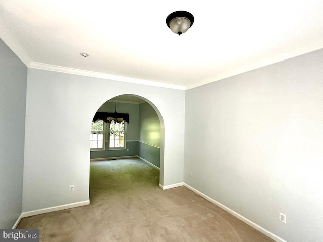 empty room with arched walkways, baseboards, crown molding, and carpet