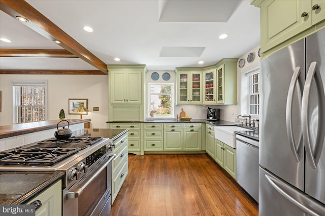 kitchen featuring a sink, dark countertops, appliances with stainless steel finishes, green cabinets, and dark wood-style flooring