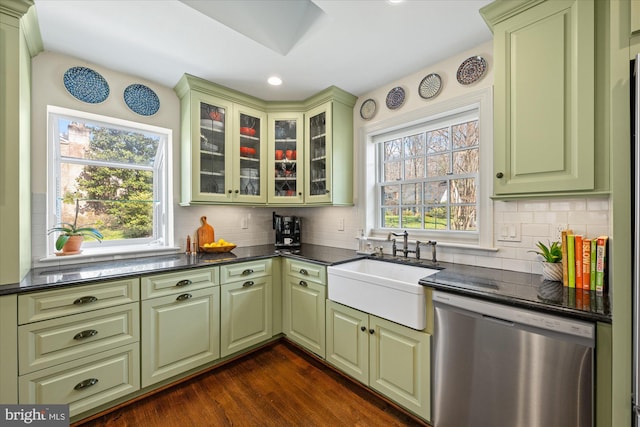 kitchen featuring green cabinetry, a sink, stainless steel dishwasher, dark countertops, and tasteful backsplash