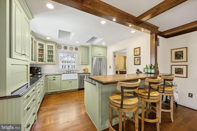 kitchen featuring beamed ceiling, a peninsula, a skylight, stainless steel appliances, and a sink