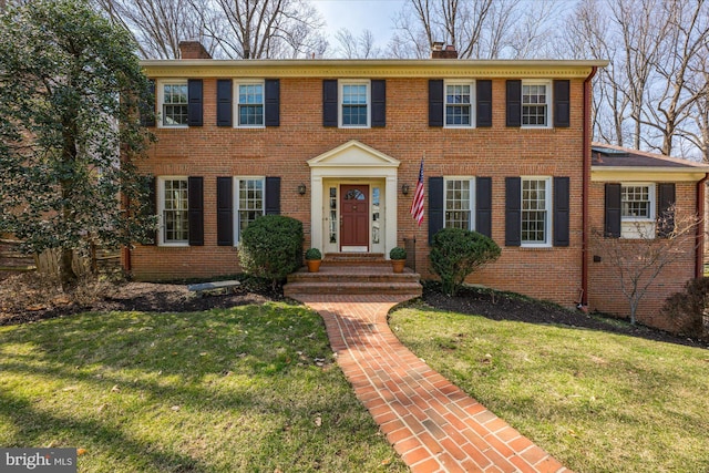 view of front of home featuring a front yard, brick siding, and a chimney