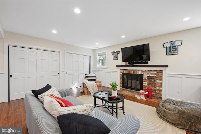 living room featuring a decorative wall, recessed lighting, a brick fireplace, and wood finished floors