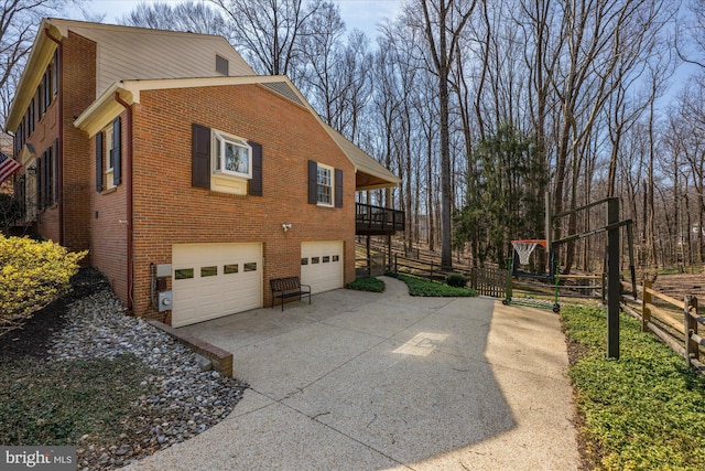 view of property exterior featuring brick siding, an attached garage, concrete driveway, and fence