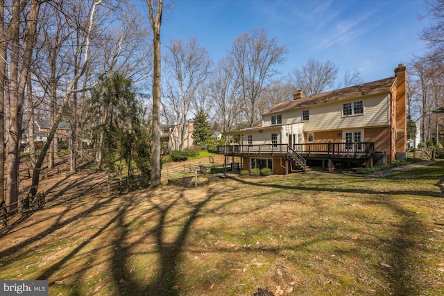 rear view of property featuring brick siding, fence, a chimney, a deck, and a yard