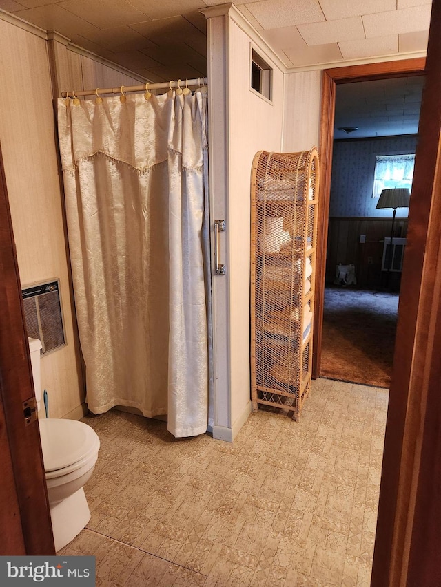 bathroom featuring tile patterned floors, toilet, a shower with shower curtain, wooden walls, and wainscoting