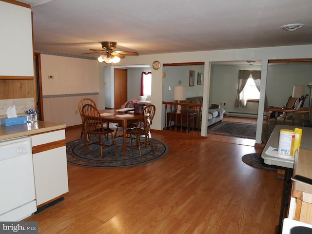 dining room with light wood finished floors, wainscoting, a baseboard heating unit, and a ceiling fan