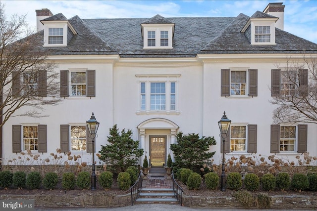 view of front of house featuring stucco siding, a high end roof, and a chimney