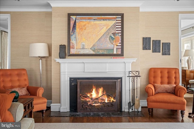 sitting room with wood finished floors, a warm lit fireplace, and ornamental molding