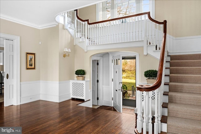 foyer with wood finished floors, arched walkways, wainscoting, crown molding, and a towering ceiling