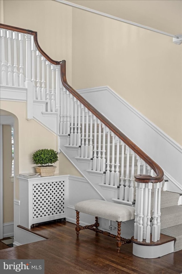 stairway featuring arched walkways and wood finished floors