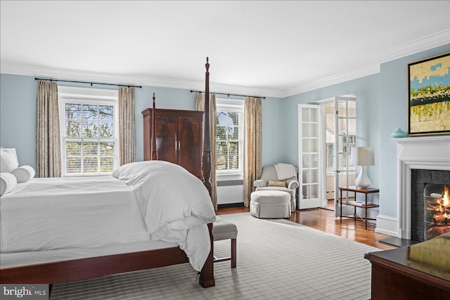 bedroom featuring wood finished floors, baseboards, a warm lit fireplace, and ornamental molding