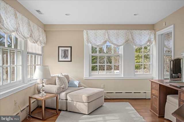 living area with a baseboard heating unit, wood finished floors, visible vents, and baseboard heating