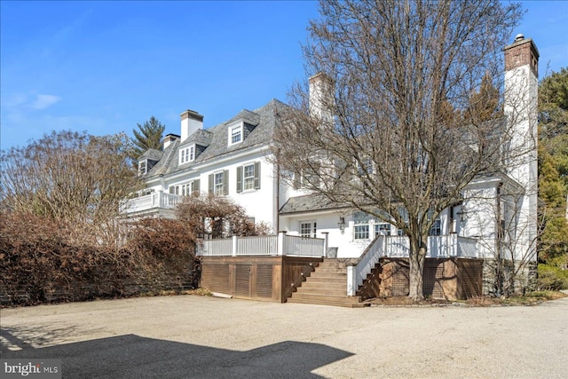 view of front facade featuring a wooden deck, stairway, and a chimney