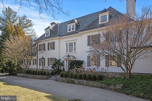 view of front facade with a high end roof, stucco siding, and a chimney