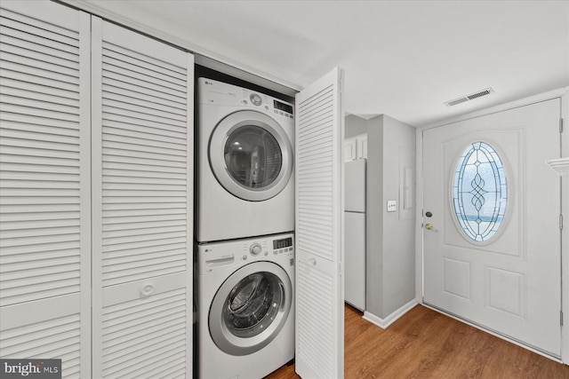 washroom featuring laundry area, baseboards, visible vents, stacked washer and clothes dryer, and wood finished floors