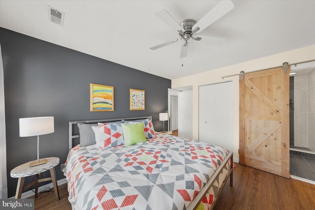 bedroom featuring a barn door, a closet, wood finished floors, and visible vents