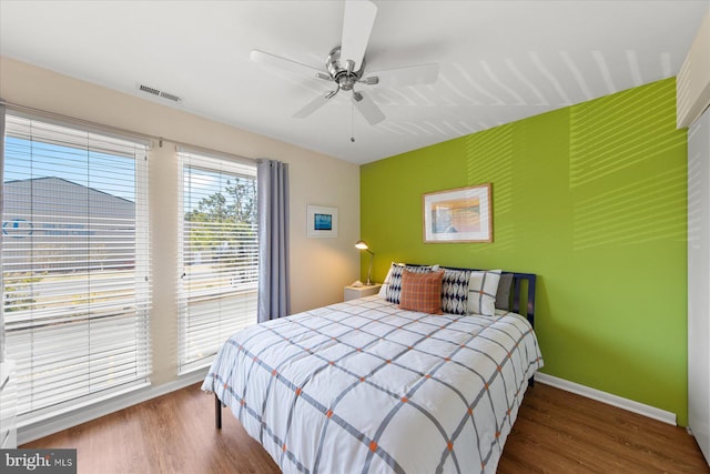 bedroom featuring a ceiling fan, visible vents, baseboards, and wood finished floors