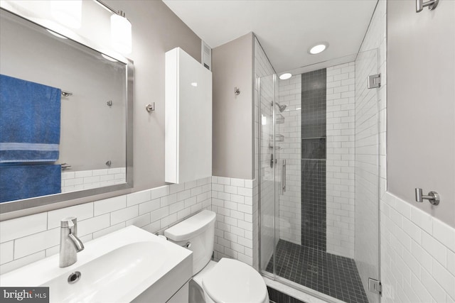 bathroom with toilet, vanity, tile walls, wainscoting, and a shower stall